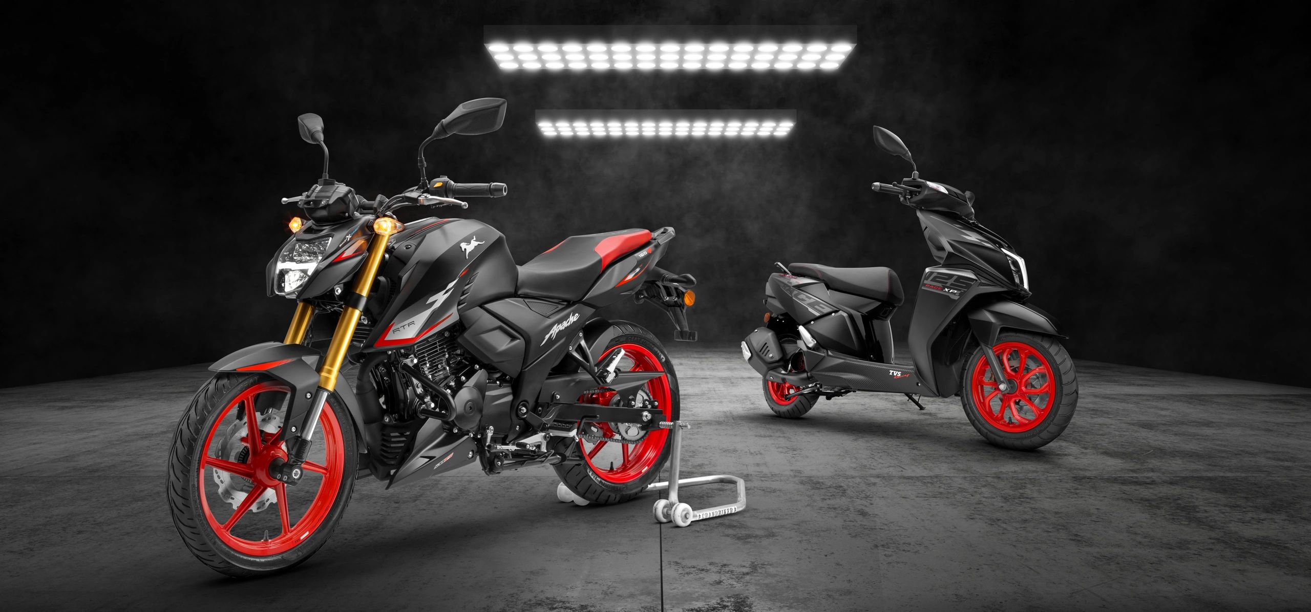 Two stylish black motorcycles with striking red rims in a dark, illuminated showroom.
