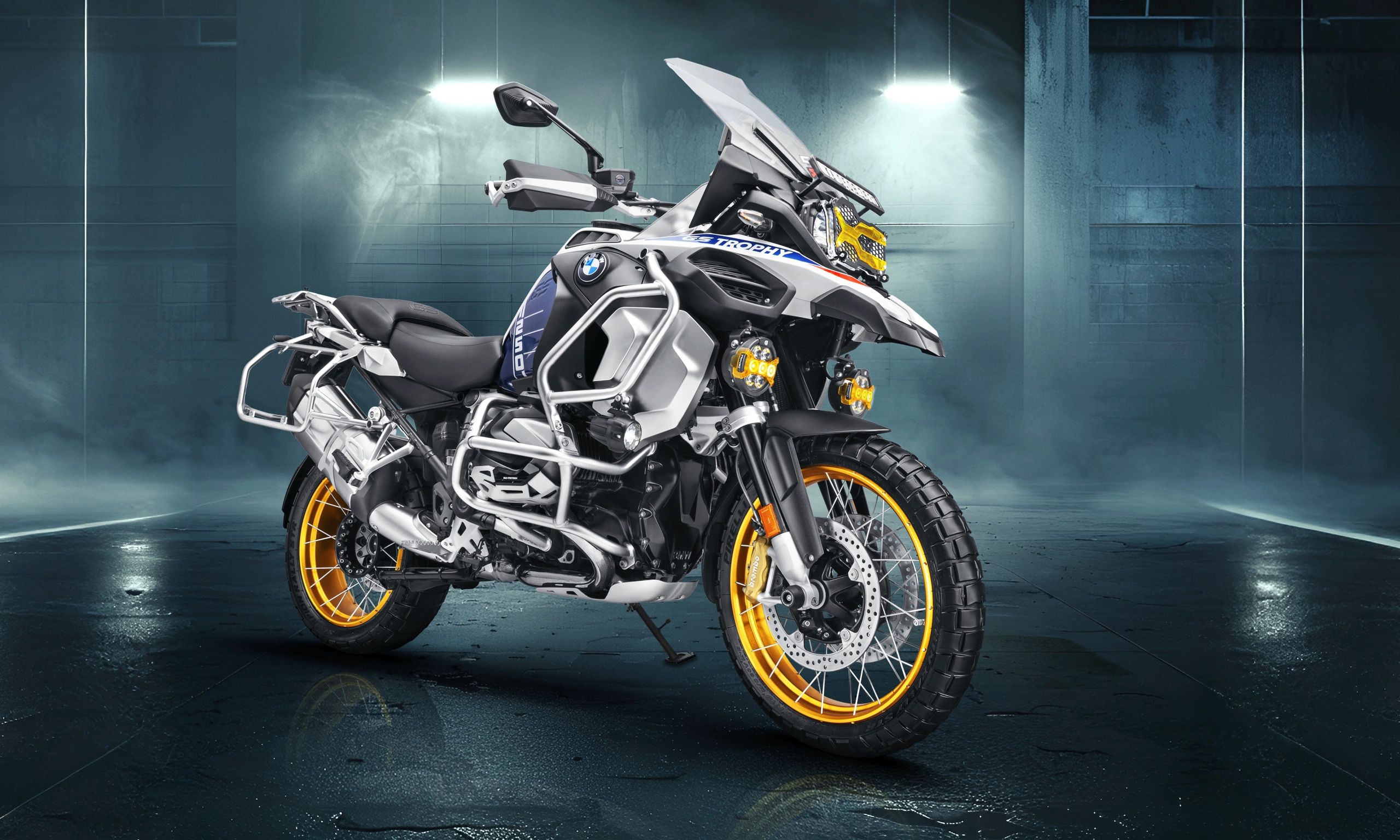 BMW adventure motorcycle with yellow rims in a moody indoor setting.