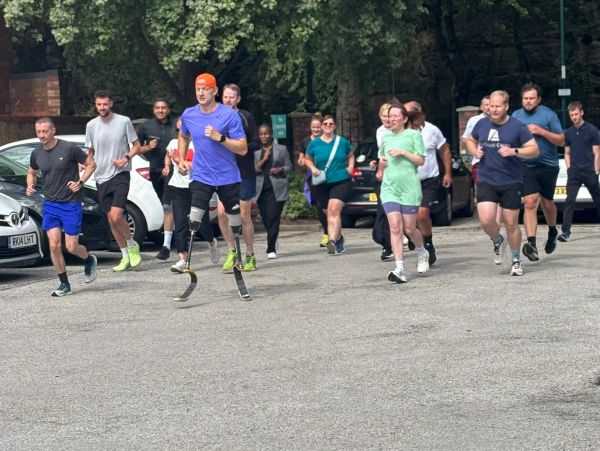 Group of people jogging outdoors, one with prosthetic running blades.