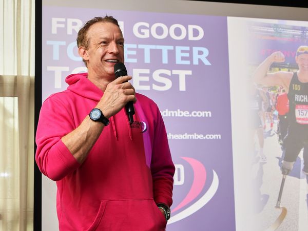 Man in pink hoodie giving a speech with a microphone.