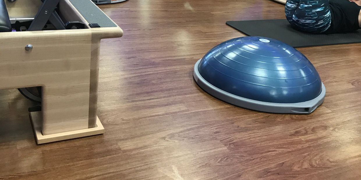 Blue balance trainer on wooden gym floor with person exercising on mat.