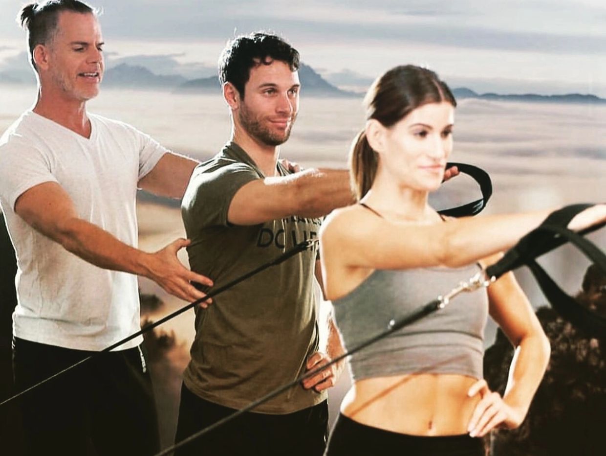 Three people exercising with resistance bands under instructor supervision.