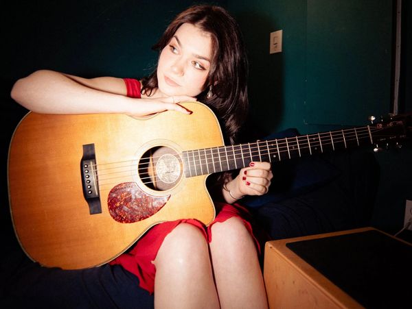 Woman in red dress holding an acoustic guitar.