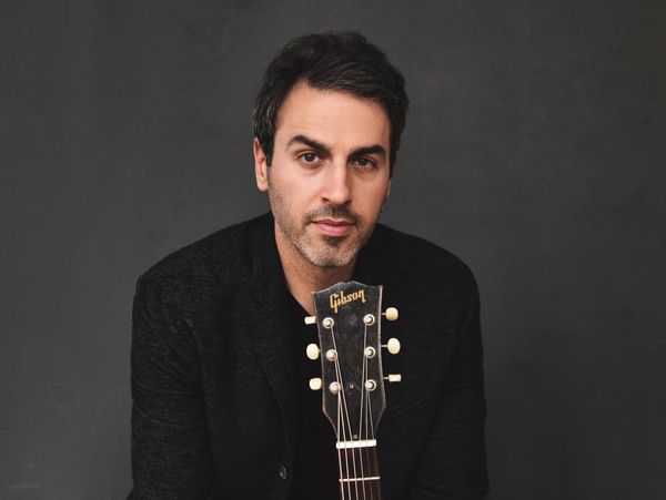 Man posing with a Gibson guitar against a dark background.