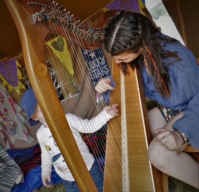 Grace in a festival setting, showing a toddler the strings on the harp. 