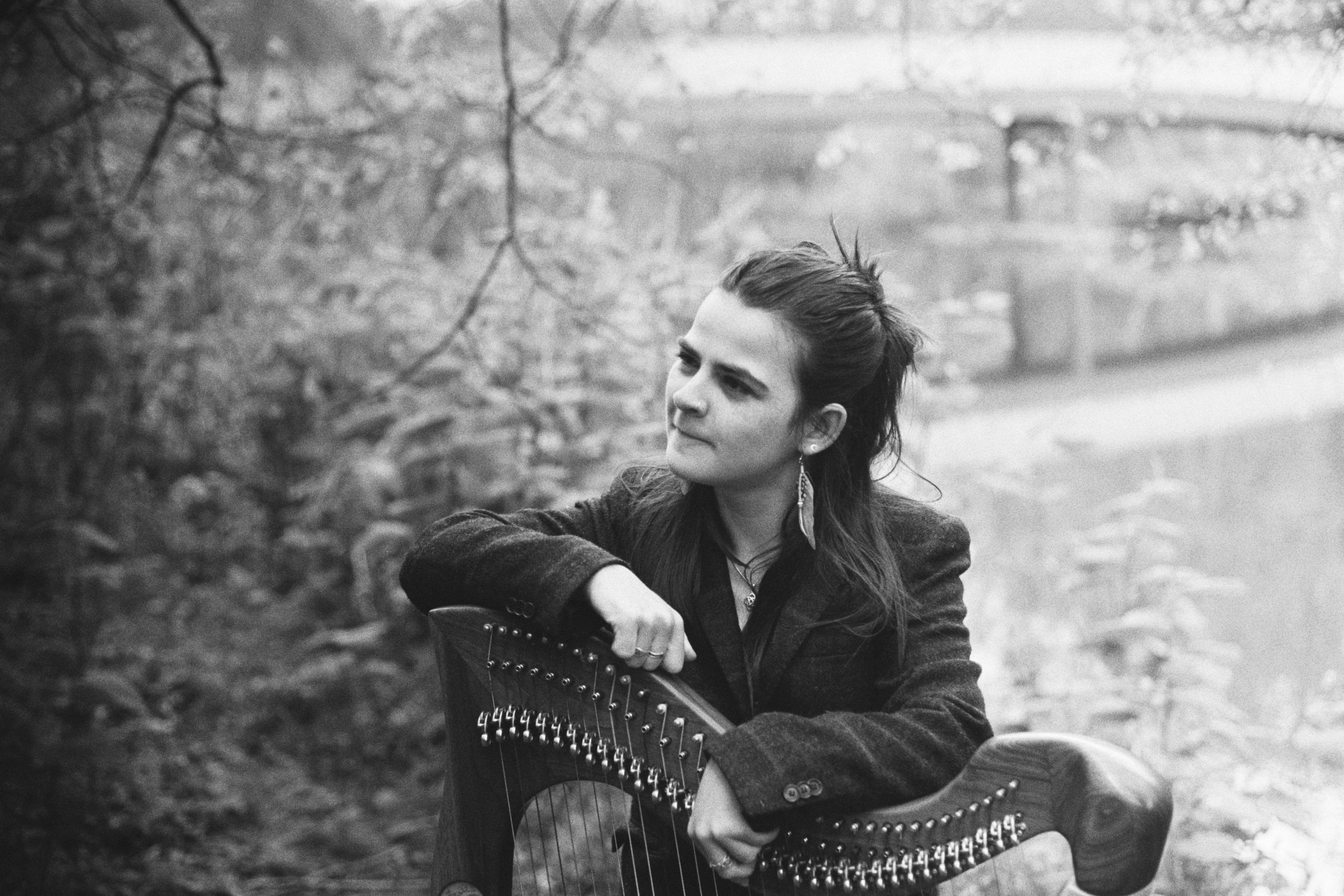 Black and white headshot. Grace leaning both arms on top of her harp and looking off to the left.