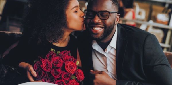Couple with the woman holding roses and kissing man on the cheek.