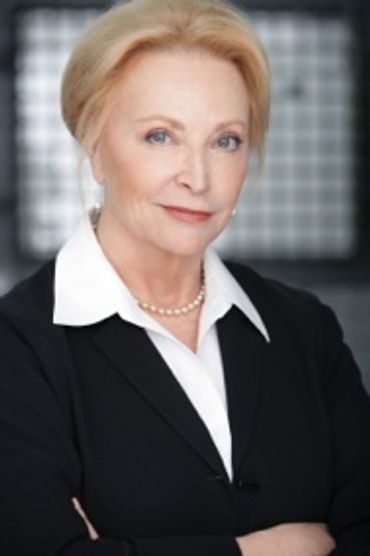 Confident older woman dressed professionally posing with arms crossed.