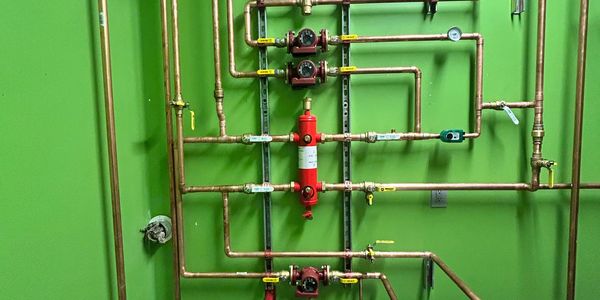 Copper piping system with red valves and green wall.