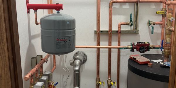 Copper piping in a water system setup with a gray tank.