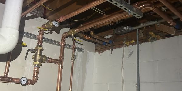 Copper pipes and gauges in a basement ceiling.