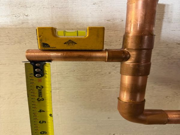 Copper pipe with measuring tape and level on a wooden surface.