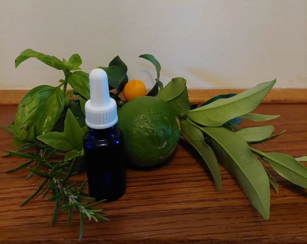 A dark blue dropper bottle surrounded by fresh green leaves and citrus fruits on a wooden surface.