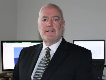 Professional man in suit standing in office with computers in background.