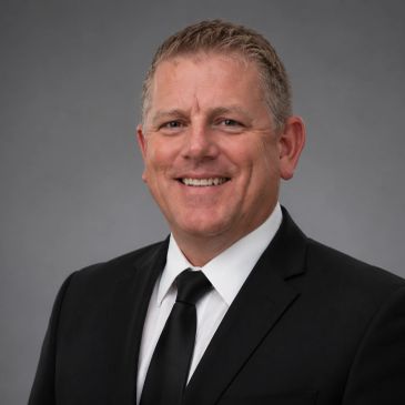 Smiling man in a black suit and tie.