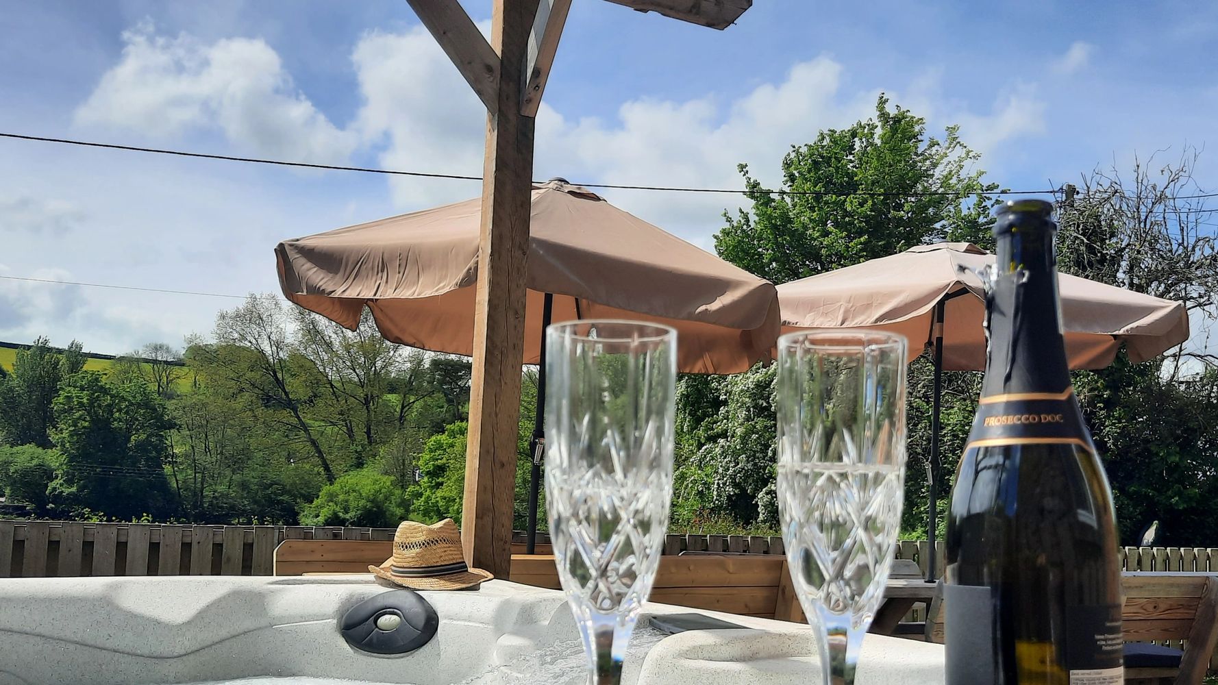 Two empty crystal glasses and a prosecco bottle by a bubbling hot tub outdoors.