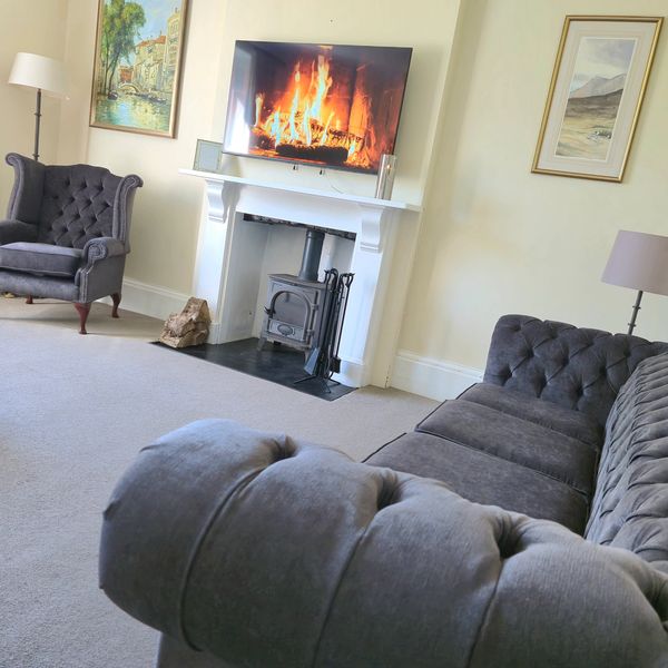 Sophisticated Chesterfield grey sofa, fire scene on tv over fireplace, arm chair in corner, artwork.