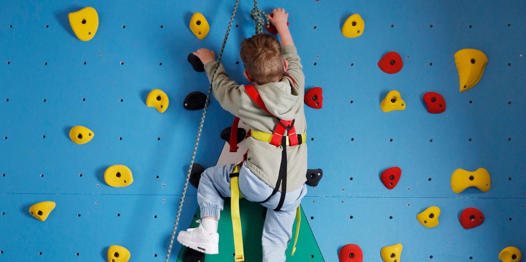 Kid with disability climbing rock wall with physiotherapist during intensive physiotherapy 