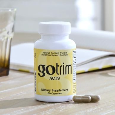 Bottle of Gotrim ACTS dietary supplement with two capsules on a wooden table.