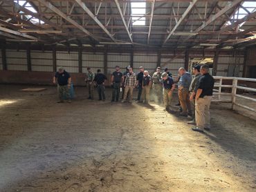 Group of people standing inside a barn or stable.