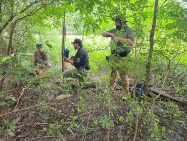 Three men in a forested area.
