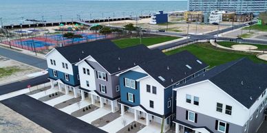 Row of modern townhouses near a beach with a playground and pier in the background.