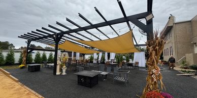 Outdoor seating area with pergola and yellow sunshade under cloudy sky.