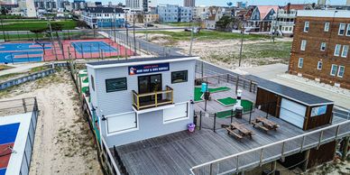 Mini golf and bike rental building with outdoor seating on a wooden deck near basketball courts.