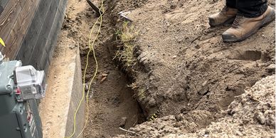 Person digging a trench near a house foundation with a shovel and yellow string line.