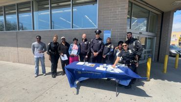 Police officers and community members gather outside a building with an information table.