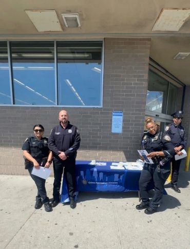 Four police officers stand near a crime prevention information table outside a building.