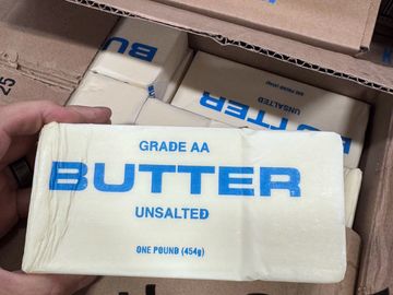 A hand holding a one-pound unsalted butter package labeled Grade AA.