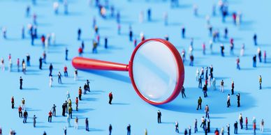 A magnifying glass focusing on small people figures scattered on a blue surface.