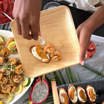 Hand placing shrimp appetizer on a wooden plate at a seafood spread.