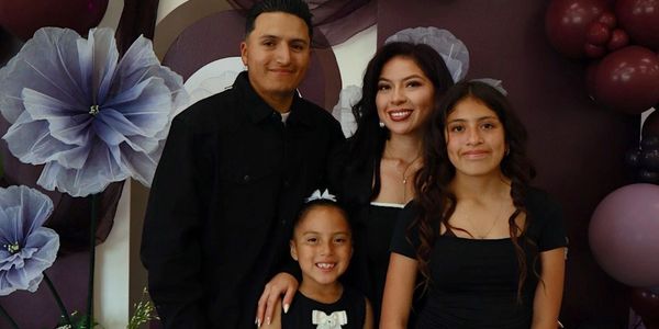 A family of four posing happily in front of purple decorations.