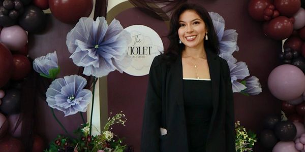 A smiling woman stands in front of a floral and balloon backdrop.
