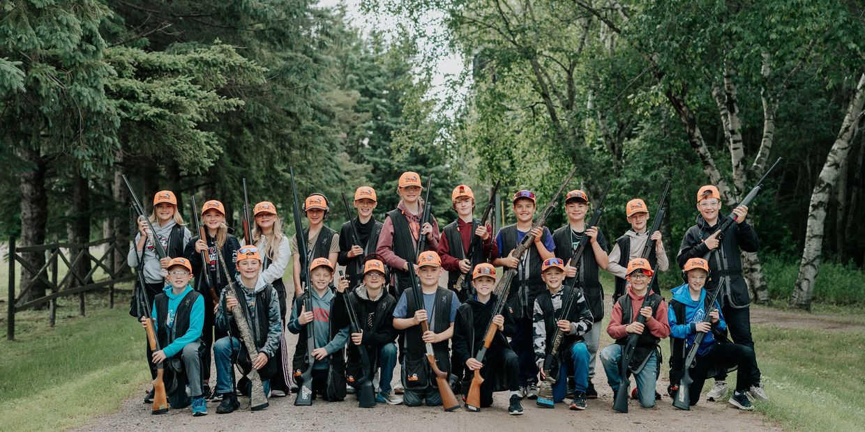 A group of kids with orange hats holding rifles in a forest clearing.