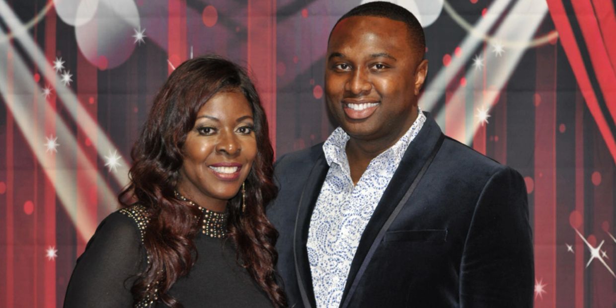 A smiling couple dressed formally in front of a decorative backdrop.