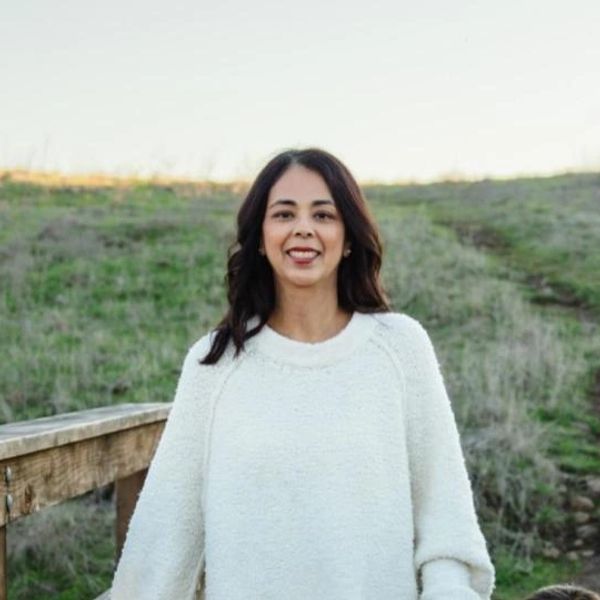 Woman smiling outdoors in a white sweater.