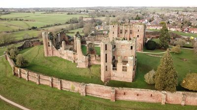 Aerial view of an ancient ruined castle surrounded by green fields and a village.