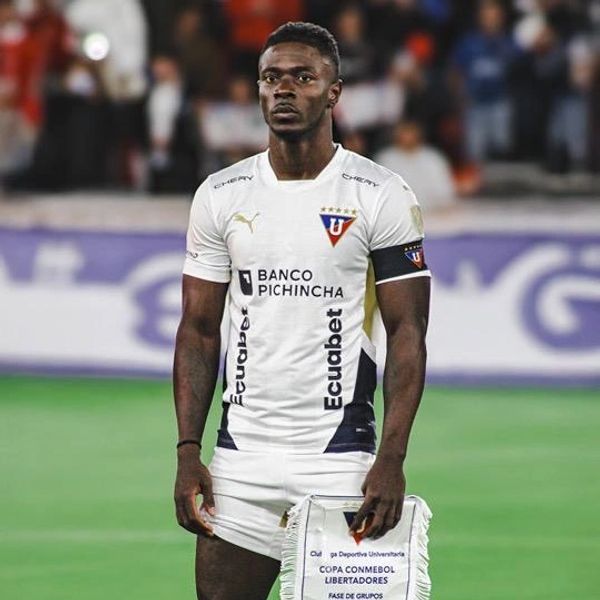 Soccer player in white uniform holding a Copa Libertadores pennant on the field.