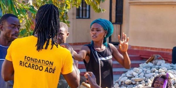 A woman gestures while talking to a man in a yellow shirt outdoors.