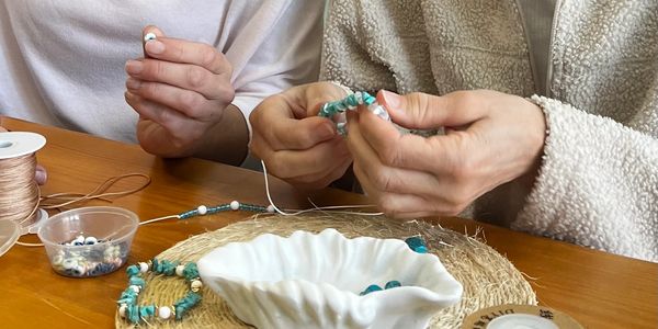 Two people making beaded bracelets with blue and white beads.