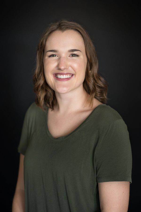 Smiling woman with wavy hair in a green shirt against a black background.