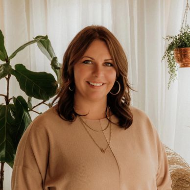 Smiling woman in beige sweater with plants in the background.