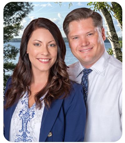 Smiling couple posing outdoors near water and trees.
