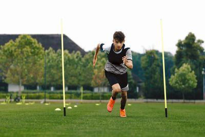 A boy sprinting through agility poles on a grass field.
