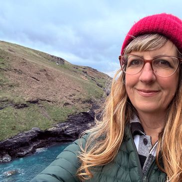 Woman in a red beanie takes a selfie near a rocky coastline.