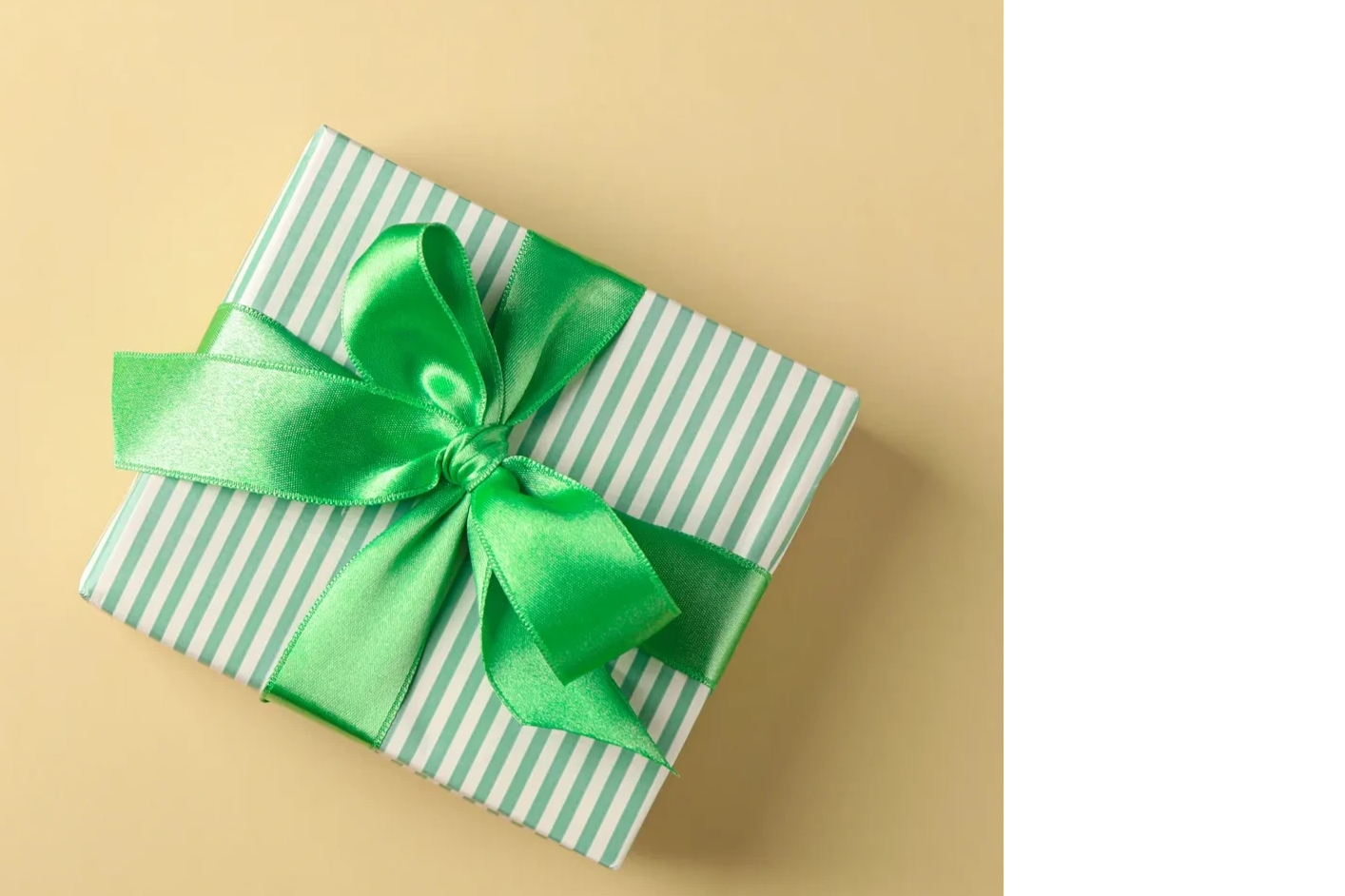 Gift box with green ribbon on beige background.