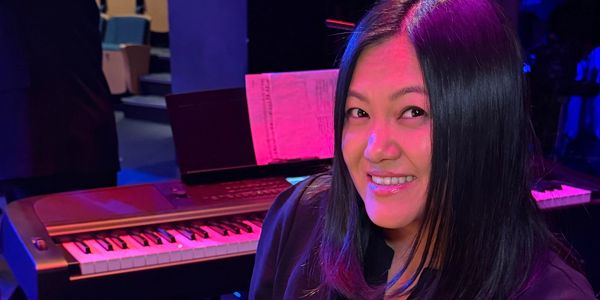 Woman smiling by a keyboard with colorful lighting.